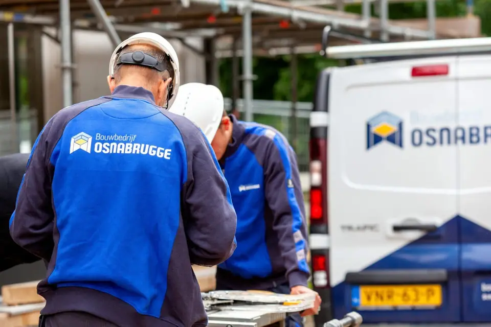 Collega's van Osnabrugge in overleg bij de bus op de bouwplaats