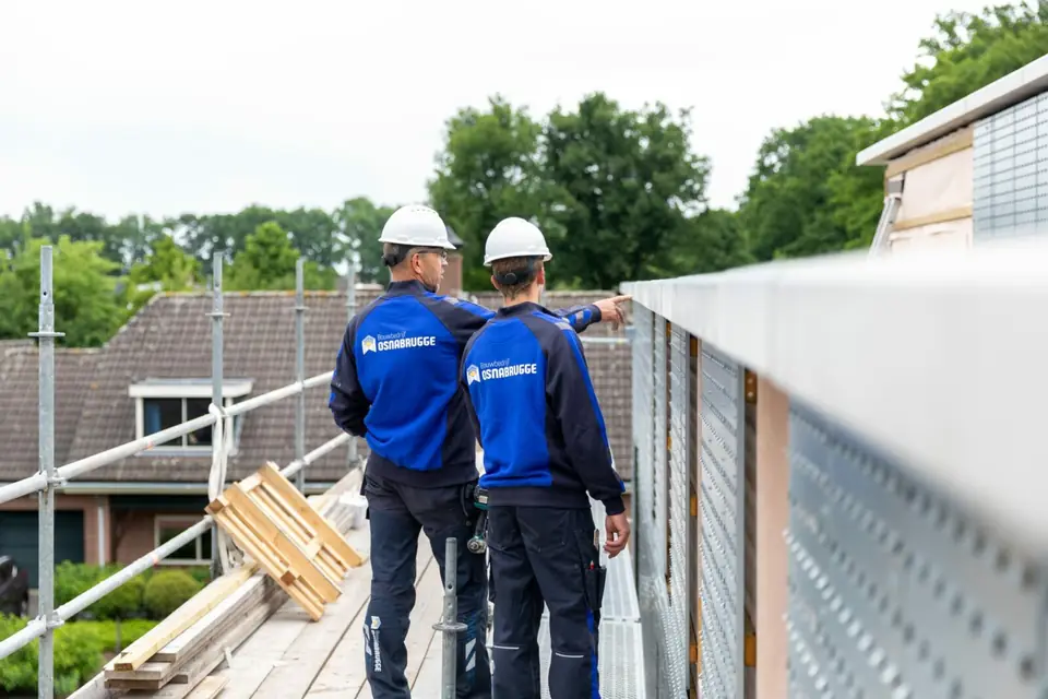 Twee collega's van Osnabrugge met bouwhelm langs de gevel van een woning in aanbouw